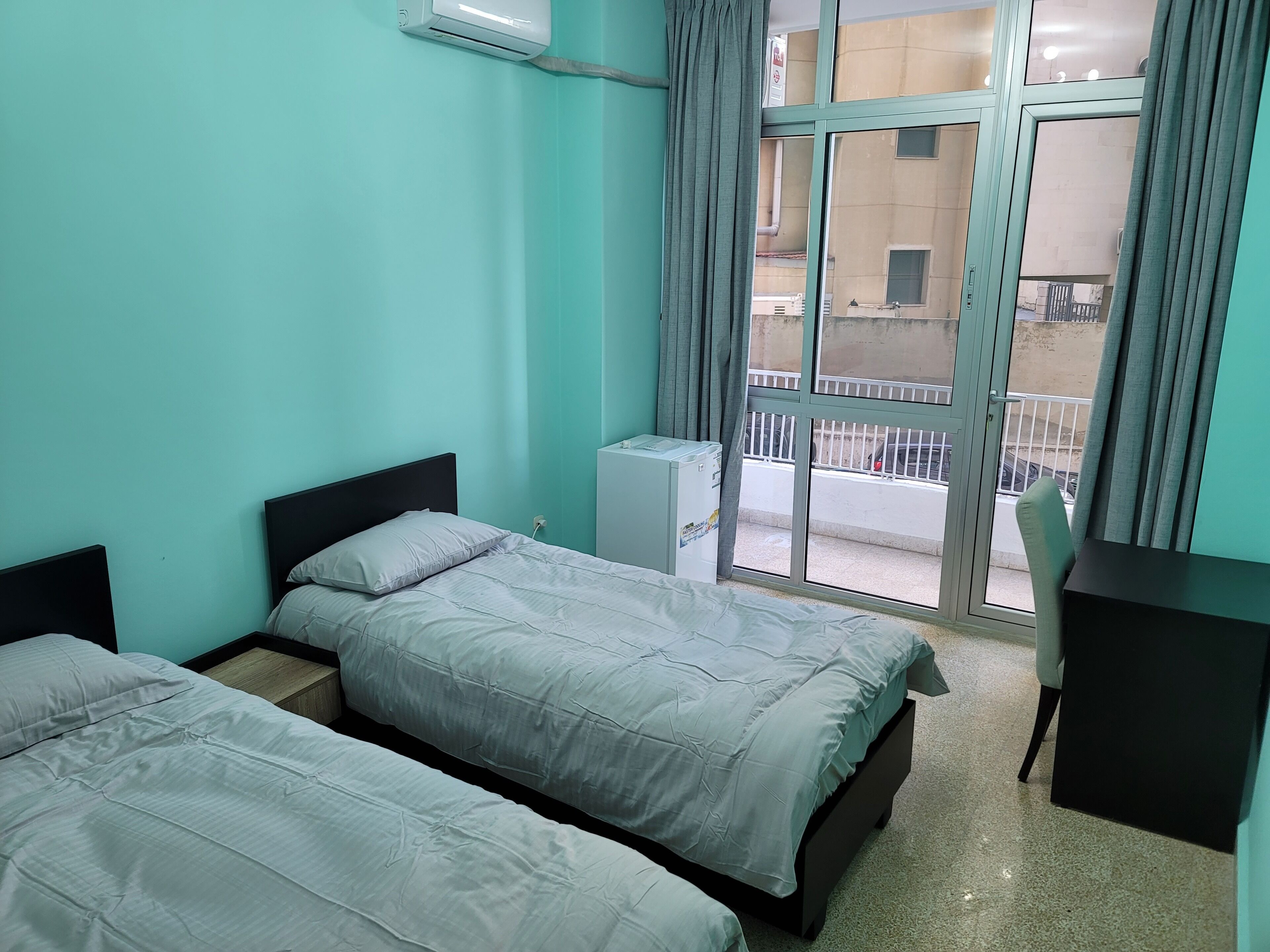 A room with two beds, a desk, and a window with a view of the outside.