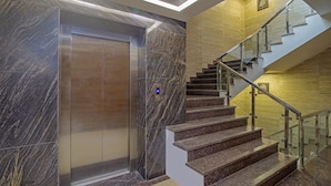 Un ascenseur moderne doté d’un écran numérique, de murs en marbre et d’un escalier avec des rampes en verre.