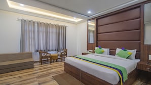 Une chambre d’hôtel avec un lit en bois, une table de chevet en bois, une petite table, une chaise, un petit canapé et une fenêtre avec des rideaux.