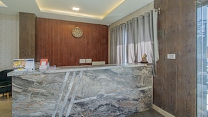 Un comptoir d’accueil avec un plateau en marbre, un lambris en bois sur le mur, une horloge et une fenêtre avec des rideaux.