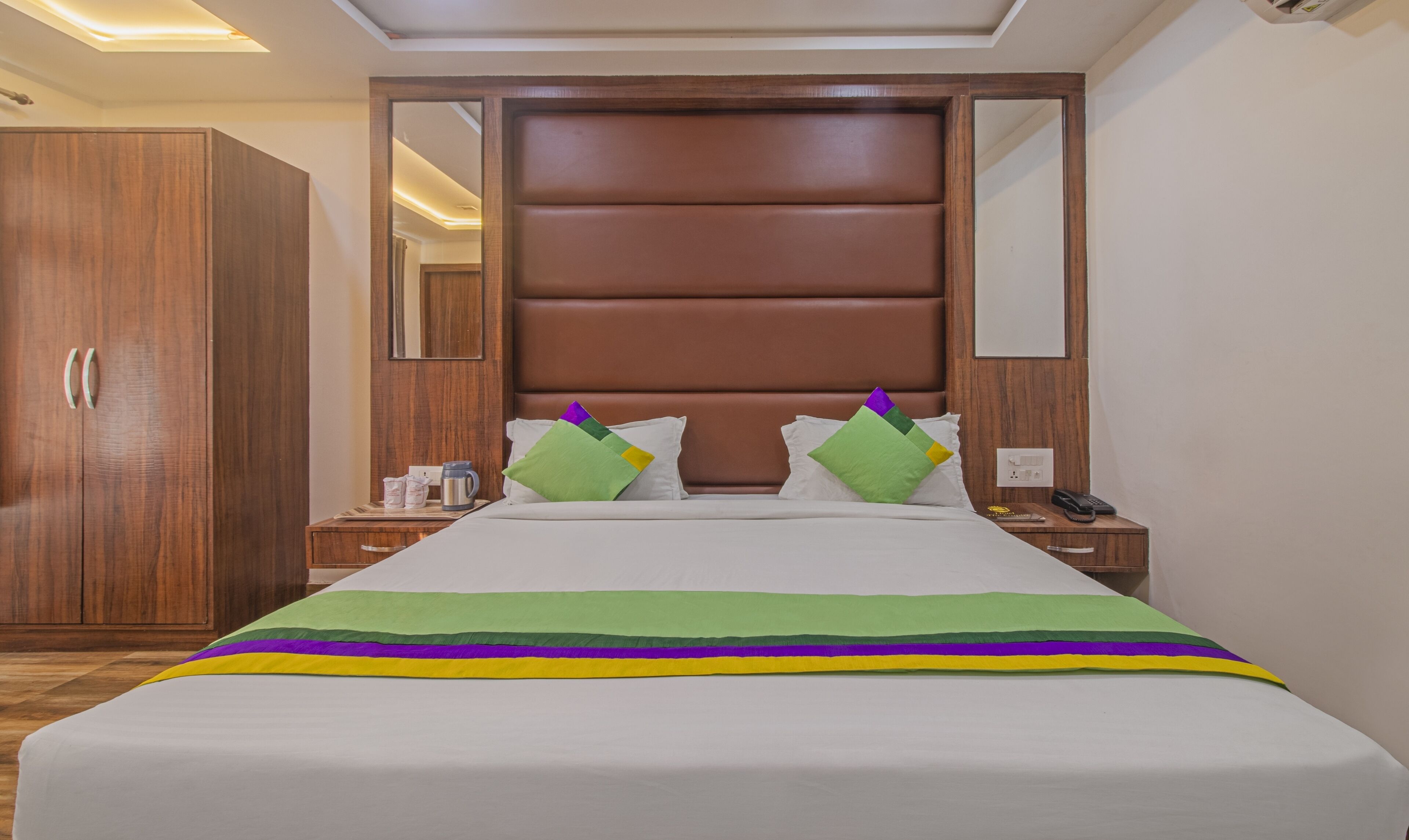 Una habitación de hotel con una cama grande, un armario de madera, mesitas de noche y un espejo.