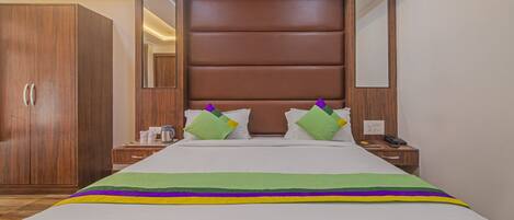 Una habitación de hotel con una cama grande, un armario de madera, mesitas de noche y un espejo.