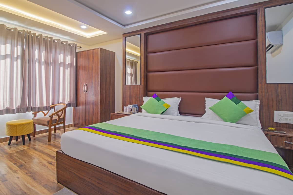 Una habitación de hotel con cabecera de madera, una cama con colcha colorida, un armario de madera, una silla y un escritorio con lámpara.