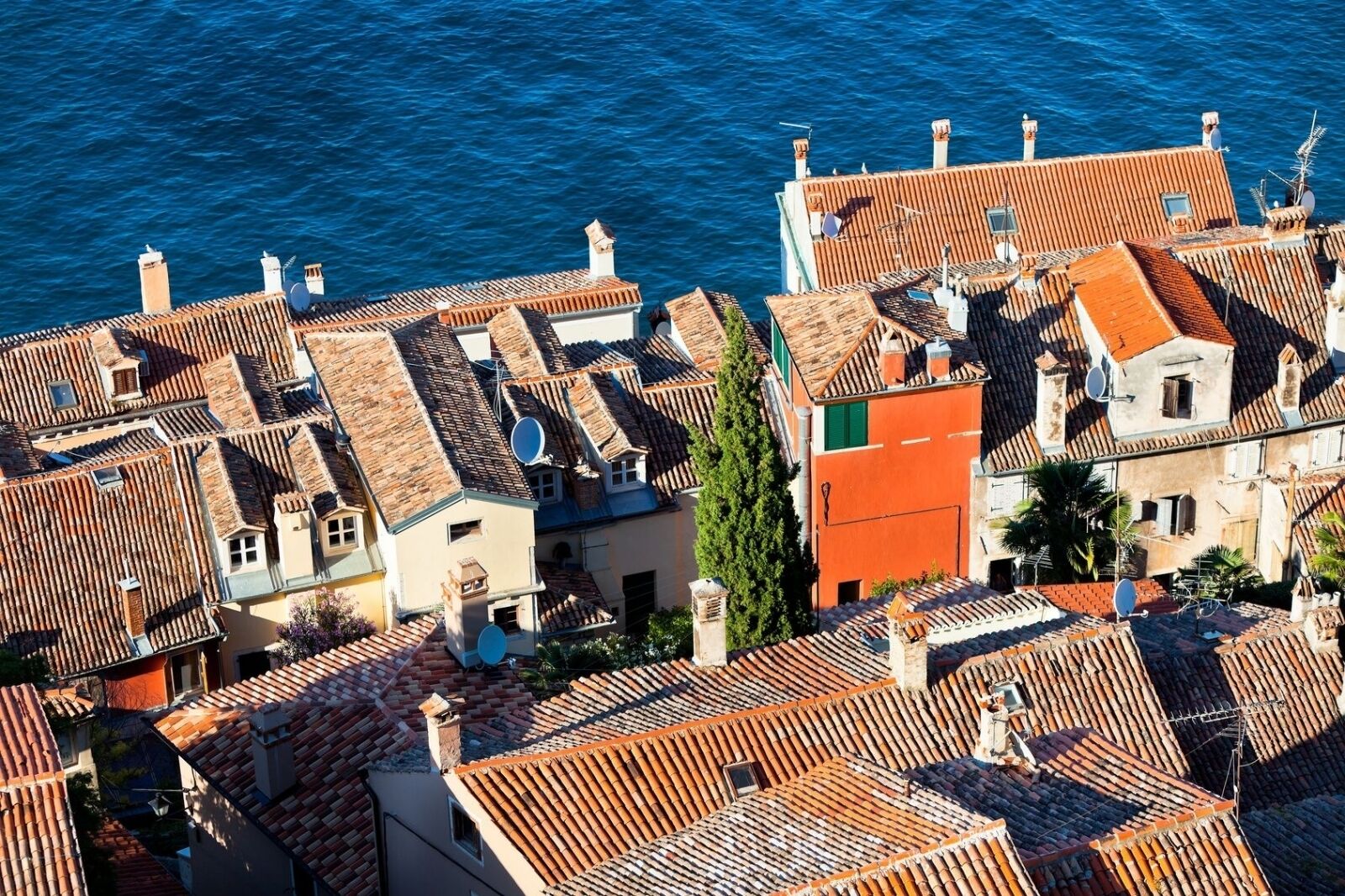 A coastal town with terracotta-tiled rooftops and buildings with balconies overlooking the sea.
