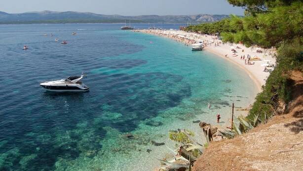 A coastal beach with clear turquoise waters, a boat, and a sandy shore with people. - Apartment in Bol with Seaview, Terrace, Air condition, WIFI (5121-2) (Bol)