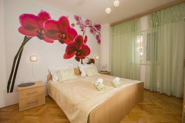A bedroom with a large bed, a nightstand, and a wall-mounted orchid mural.