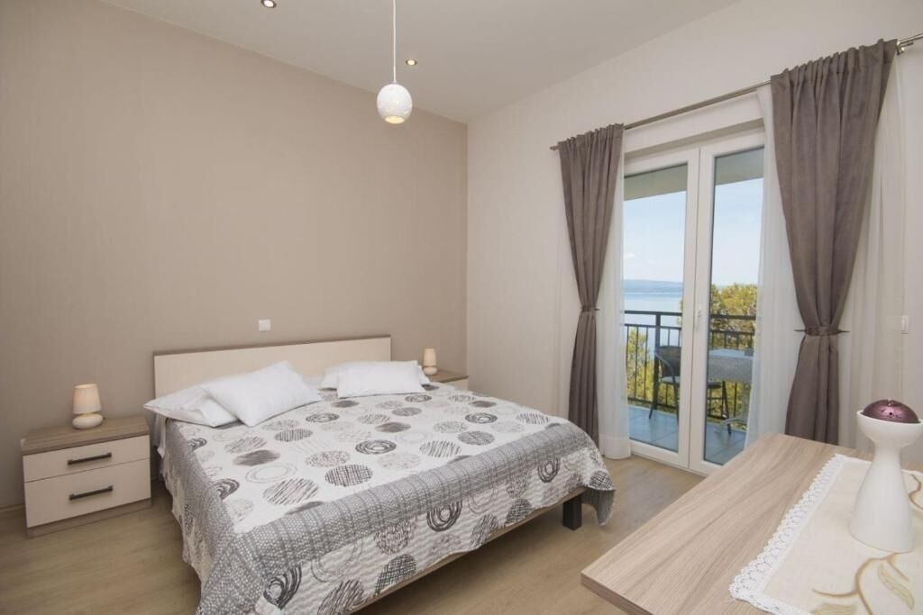 Ein Schlafzimmer mit Bett, Nachttischen, Vorhängen an einem Fenster und Blick ins Freie.