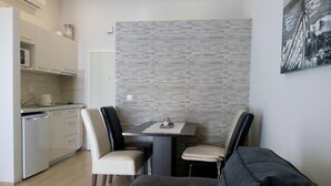 A compact living space with a kitchenette, a dining table with two chairs, and a gray sofa.