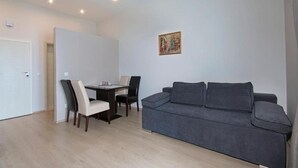 A modern living room with a grey sofa, a dining table with chairs, and a painting on the wall.
