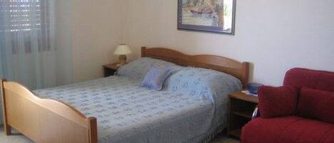 Un dormitorio con una cama, una mesita de noche, un sofá rojo, una ventana con persianas y un cuadro en la pared.