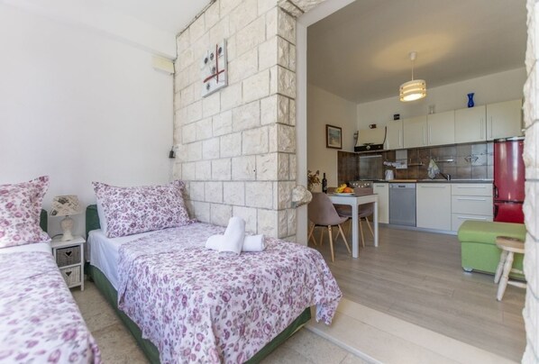 A bedroom with a bed, a nightstand, and a wall clock. There is a kitchen area with a dining table, chairs, and cabinets.