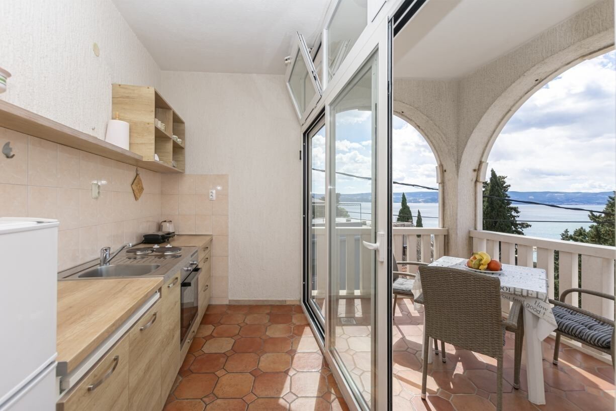 Un balcón con vista al mar, una mesa de comedor con sillas y una zona de cocina con fregadero y armarios.