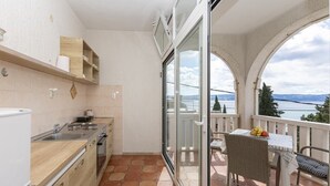 Un balcón con vista al mar, una mesa de comedor con sillas y una zona de cocina con fregadero y armarios.