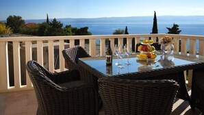 A balcony with wicker furniture and a glass table set for dining, overlooking a scenic view of the sea. - Apartment in Omiš with Seaview, Terrace, Air condition, WIFI (5129-6) (Omiš)