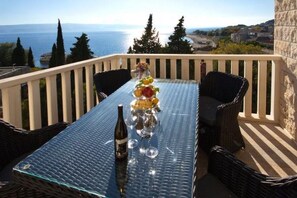 Een balkon met rieten meubels, een glazen tafel en een fles wijn.