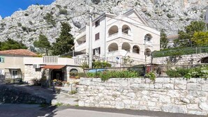 A multi-story building with a stone facade, arched windows, and a balcony. It is situated in a mountainous area with rocky terrain in the background. - Apartment in Omiš with Seaview, Terrace, Air condition, WIFI (5129-2) (Omiš)