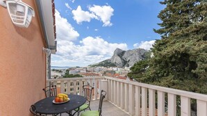 A balcony with a table and chairs, a fruit bowl, and a view of a mountain and cityscape. - Apartment in Omiš with Seaview, Balcony, Air condition, WIFI (5129-5) (Omiš)