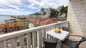 Un balcón con mesa y sillas, con vistas a un pueblo costero con edificios y montañas.