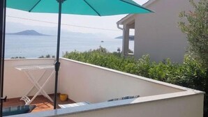 A balcony with a white table and a green umbrella, overlooking a body of water and a distant mountain. - Apartment in Slatine with Seaview, Balcony, Air condition, WIFI (5130-1) (Slatine)