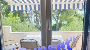 A view through a glass door to an outdoor patio area with a striped awning and a table with chairs. - Apartment in Slatine with Seaview, Balcony, Air condition, WIFI (5130-1) (Slatine)