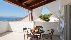 Ein Balkon mit Korbstühlen, einem Tisch mit Frühstücksgebäck und Blick auf das Meer und die Berge.