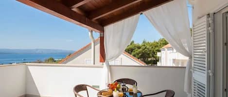 A balcony with wicker chairs, a table with breakfast items, and a view of the sea and mountains.