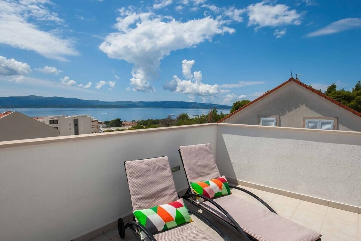 Un balcón con dos sillones de descanso, uno con un cojín de colores y otro con un cojín liso, con vistas a una masa de agua y colinas a lo lejos.