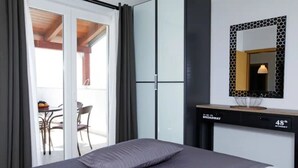 Ein modernes Hotelzimmer mit Bett, Schminktisch, Spiegel und einer Glastür zum Balkon.