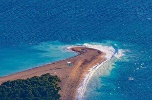 Una vista aerea di una spiaggia con un litorale curvo, una piccola costruzione e una zona boschiva.
