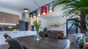 A modern kitchen with white cabinets, a dark countertop, and a vase with flowers. There is a dining area with a dark table and chairs, and a living room with a sofa and a painting on the wall. - Apartment in Bol with Seaview, Balcony, Air condition, WIFI (5127-1) (Bol)
