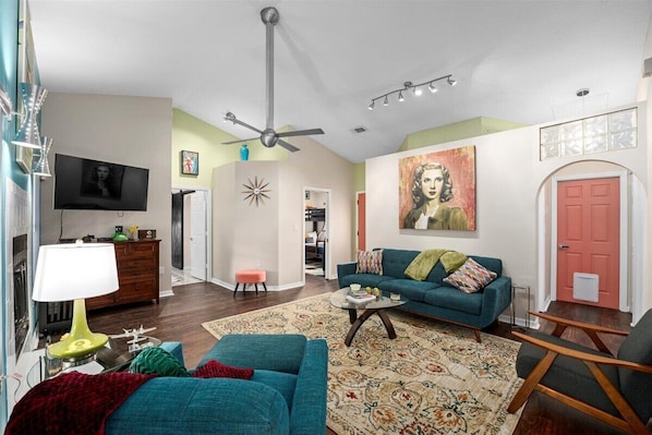 A living room with a teal sofa, a coffee table, a TV, and a ceiling fan.
