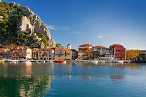 Une ville côtière avec des bâtiments le long du front de mer, des bateaux amarrés et une falaise rocheuse imposante en arrière-plan.