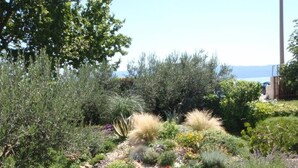A garden with various plants and shrubs, a clear sky, and a distant view of the sea. - Apartment in Dugi Rat with Seaview, Balcony, Air condition, WIFI (5132-4) (Dugi Rat)