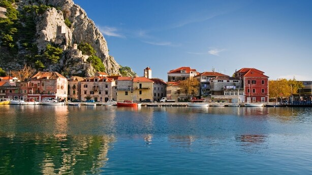 A coastal town with buildings along the waterfront, boats docked, and a prominent rocky cliff in the background. - Apartment in Dugi Rat with Seaview, Balcony, Air condition, WIFI (5132-4) (Dugi Rat)