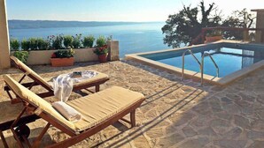 Ein Poolbereich mit Meerblick, zwei Liegestühle und Kübelpflanzen.