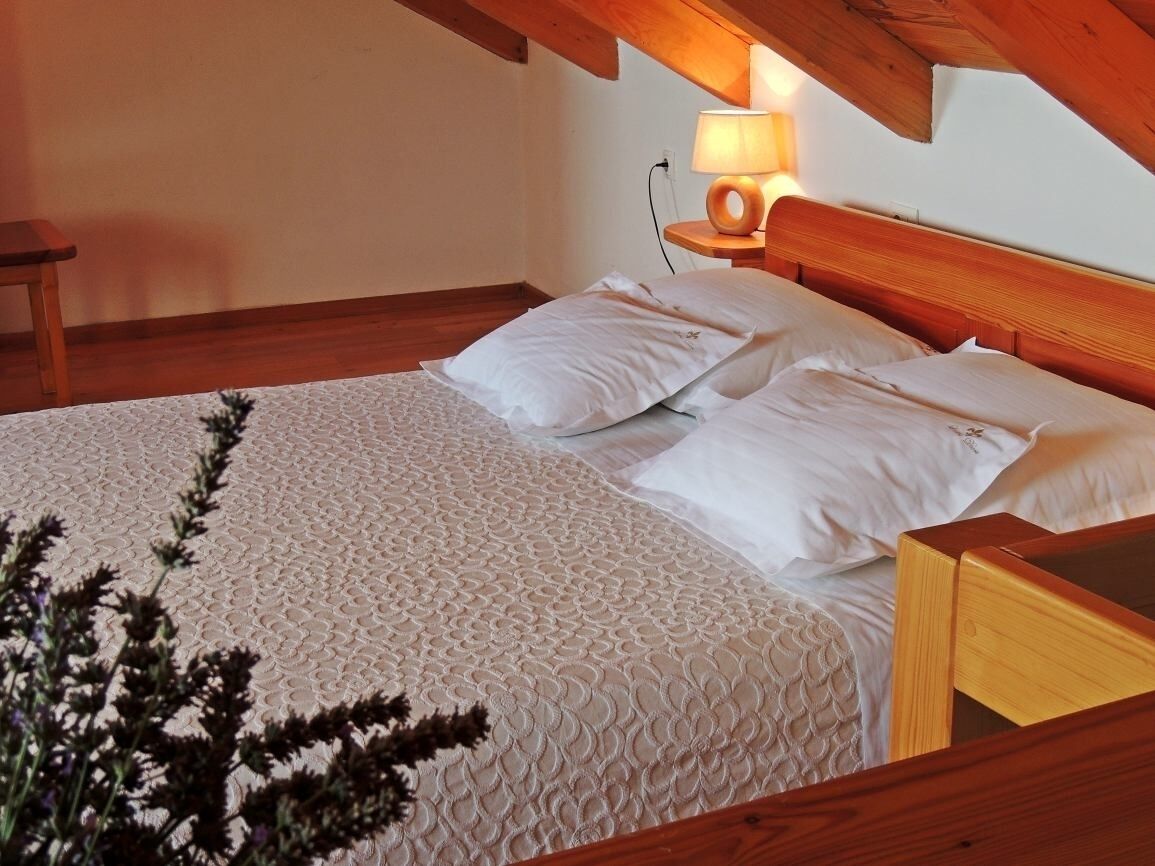 Una camera da letto con un letto con struttura in legno, un comodino con lampada e una panca in legno ai piedi del letto.