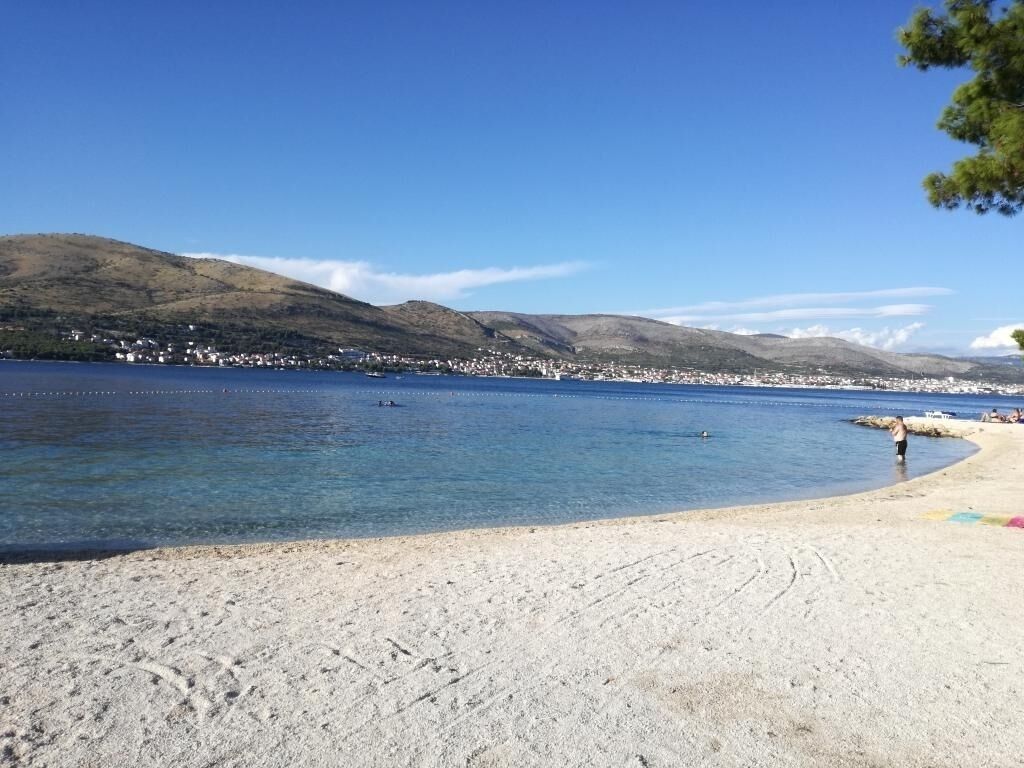 Una spiaggia con acque cristalline, una riva sabbiosa e una città sullo sfondo.
