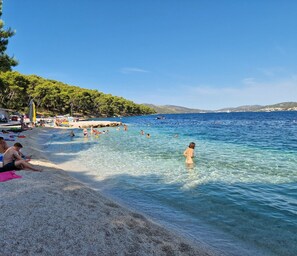 A beach with clear water, people swimming, and a sandy shore.