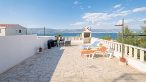 A rooftop terrace with stone flooring, outdoor seating, and a view of the sea.
