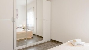 A bedroom with a large wardrobe, a bed with a white duvet, and a rolled towel on the bed.