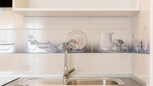 A kitchen with a stainless steel sink, white tiles, and decorative glassware.