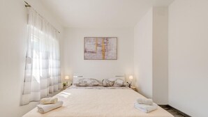 A hotel room with a large bed, a painting on the wall, and a window with sheer curtains.
