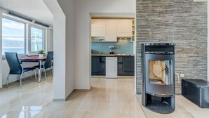 A modern kitchen with a built-in stove, a dining area with a table and chairs, and a view of the sea through large windows.