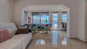 A living room with a sofa, colorful chairs, a table, and a view of the sea through large windows.