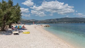 A beach with clear waters, a rocky shoreline, and mountains in the background.