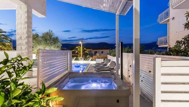A hot tub in a covered outdoor area with a pool and lounge chairs, overlooking a mountainous landscape.