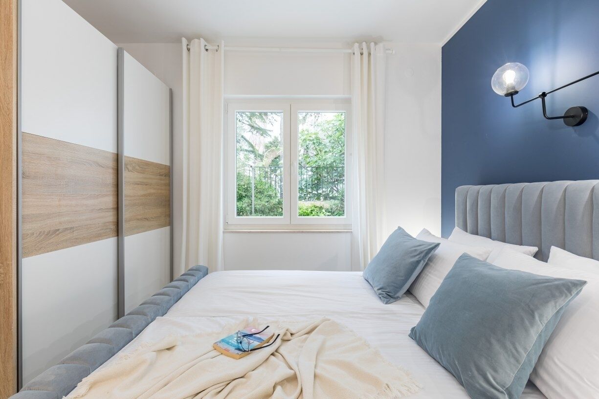Een slaapkamer met een bed, nachtkastje, raam met gordijnen en een wandlamp.