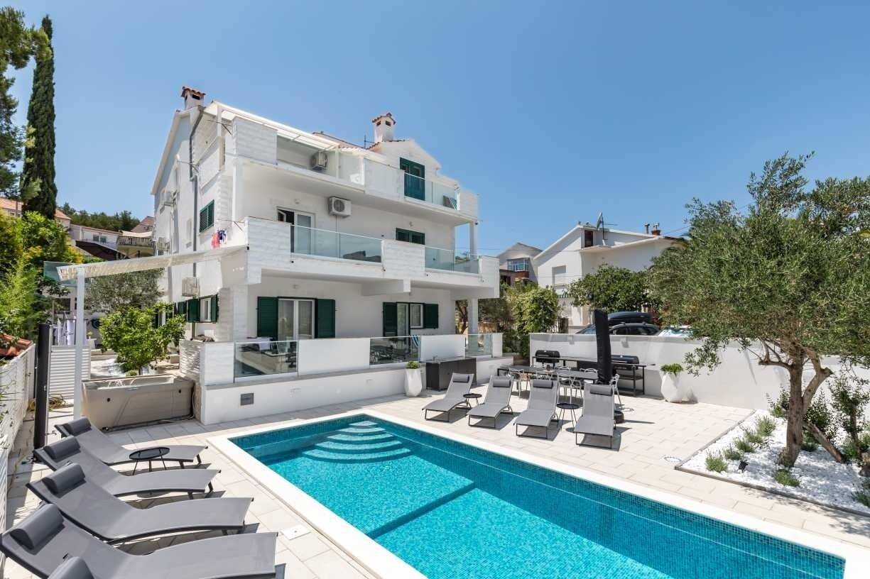 A modern two-story building with a rooftop pool area, including lounge chairs and a barbecue.