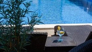 Een zwembadterras met een drankje, een stoel en een potplant.