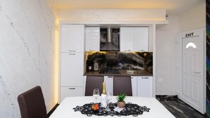 Une cuisine moderne avec des armoires blanches, un comptoir noir et un pare-feu avec un motif rappelant le marbre. On y trouve une table à manger avec un set de table, une chaise et une bouteille de champagne. Un panneau de signalisation indiquant la sortie est visible sur le mur.